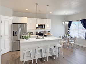 Kitchen featuring white cabinetry, stainless steel appliances, tasteful backsplash, a breakfast bar, and light wood finished floors