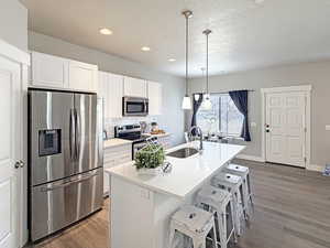 Kitchen with stainless steel appliances, white cabinetry, decorative backsplash, a kitchen bar, and decorative light fixtures