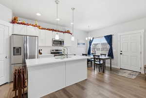 Kitchen featuring appliances with stainless steel finishes, pendant lighting, white cabinets, a center island with sink, and tasteful backsplash