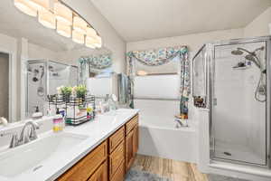 Primary bathroom featuring a bath, a stall shower, double vanity, and light wood finished floors