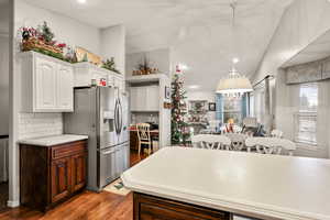 Kitchen with white cabinetry, stainless steel refrigerator with ice dispenser, vaulted ceiling, dark wood-style flooring, and decorative backsplash
