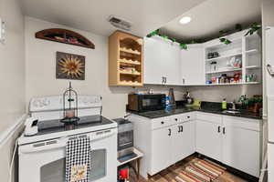Kitchenette with electric range, open shelves, white cabinets, black microwave, and dark stone countertops