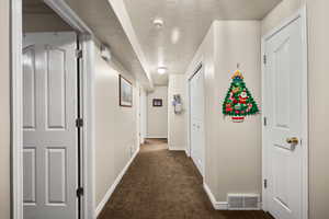 Hall featuring dark colored carpet and a textured ceiling