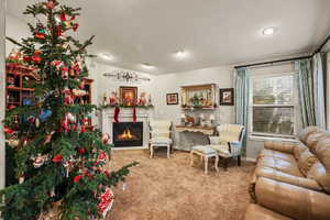 Carpeted living area featuring a warm lit fireplace and vaulted ceiling