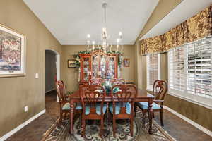 Dining space featuring arched walkways, vaulted ceiling, a chandelier, and dark colored carpet