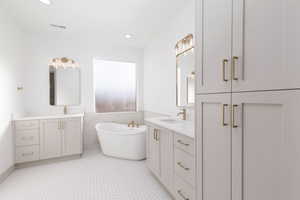 Full bathroom featuring two vanities, a soaking tub, and recessed lighting