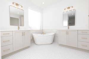 Bathroom featuring two vanities, a freestanding bath, light flooring, wainscoting, and tile walls