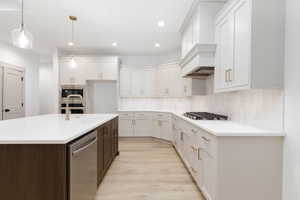 Kitchen featuring pendant lighting, stainless steel appliances, white cabinetry, recessed lighting, and a center island with sink