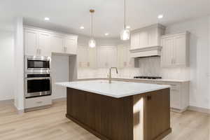 Kitchen featuring appliances with stainless steel finishes, white cabinets, decorative light fixtures, backsplash, and a kitchen island with sink