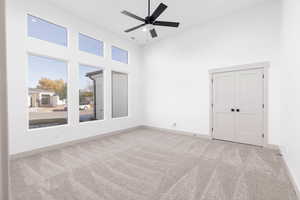 Spare room with a high ceiling, light carpet, and ceiling fan