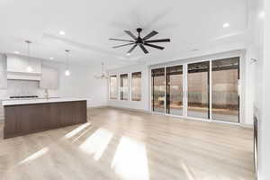 Unfurnished living room with a tray ceiling, recessed lighting, light wood finished floors, a chandelier, and a ceiling fan