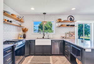 Kitchen featuring open shelves, appliances with stainless steel finishes, a peninsula, decorative light fixtures, and light stone counters