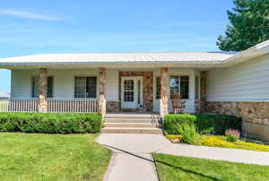 View of exterior entry featuring stone siding, a porch, a lawn, and a metal roof