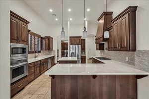 Kitchen featuring recessed lighting, a peninsula, tasteful backsplash, stainless steel appliances, and a kitchen island
