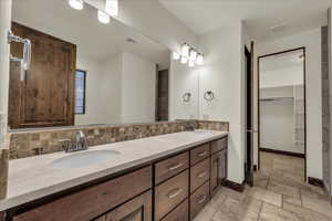 Full bath featuring stone tile floors, double vanity, a walk in closet, and tasteful backsplash