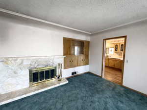 Unfurnished living room featuring a textured ceiling, a stone fireplace, ornamental molding, and dark carpet