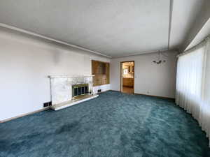 Unfurnished living room with a textured ceiling, a stone fireplace, a chandelier, and dark colored carpet