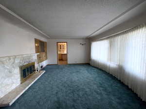 Unfurnished living room with a textured ceiling, a stone fireplace, and carpet floors