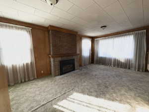 Unfurnished living room featuring a fireplace, carpet flooring, healthy amount of natural light, and wooden walls
