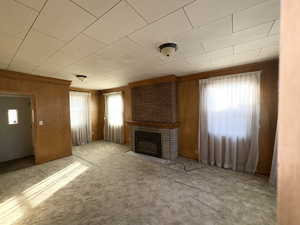 Unfurnished living room featuring a brick fireplace, carpet flooring, and wood walls