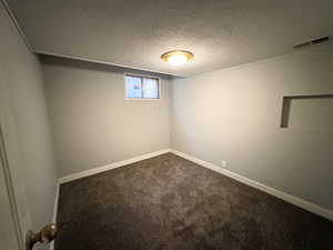 Spare room with a textured ceiling and dark colored carpet