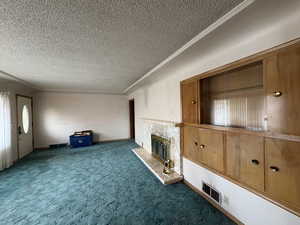 Unfurnished living room featuring crown molding, a textured ceiling, carpet flooring, and a stone fireplace