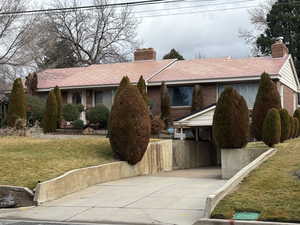 Single story home with a front lawn, brick siding, a chimney, and concrete driveway