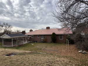 Back of house with a chimney, brick siding, and a lawn