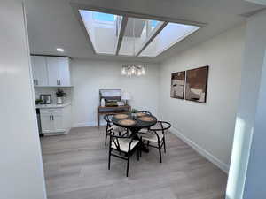 Dining room with a skylight, light wood finished floors, a chandelier, and recessed lighting