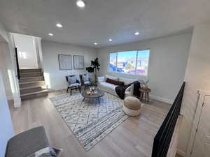 Living room with a textured ceiling, recessed lighting, light wood finished floors, and stairway