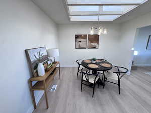 Dining area with a chandelier, light wood-style floors, and a skylight