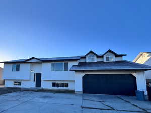 Raised ranch featuring concrete driveway, a garage, and roof with shingles