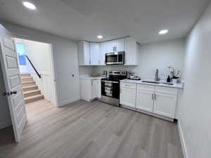 Kitchen featuring stainless steel appliances, white cabinetry, recessed lighting, light wood finished floors, and a textured ceiling