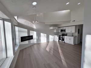Unfurnished living room with light wood-style flooring, a textured ceiling, a high ceiling, and recessed lighting
