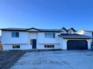 Raised ranch featuring concrete driveway, an attached garage, and roof with shingles