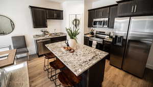 Kitchen with stainless steel appliances, light stone countertops, a center island, and dark brown cabinets