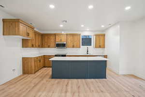 Kitchen with a center island, recessed lighting, brown cabinets, light wood finished floors, and stainless steel microwave