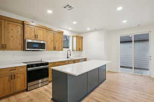 Kitchen featuring appliances with stainless steel finishes, a kitchen island, recessed lighting, light wood-type flooring, and light stone countertops