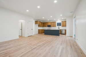 Kitchen featuring open floor plan, recessed lighting, brown cabinetry, a kitchen island, and light countertops