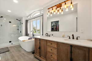 Bathroom featuring a freestanding tub, double vanity, light wood-style floors, a walk in closet, and a marble finish shower