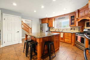 Kitchen with glass insert cabinets, a kitchen breakfast bar, appliances with stainless steel finishes, a kitchen island, and brown cabinetry