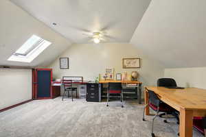 Home office with light colored carpet, vaulted ceiling, a skylight, and a ceiling fan
