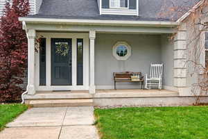 Property entrance featuring roof with shingles, a porch, and a lawn