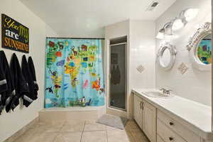 Bathroom with vanity, a stall shower, light tile patterned flooring, backsplash, and tile walls