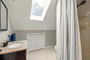 Bathroom with a skylight, lofted ceiling, vanity, and curtained shower