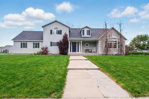 View of front of property with a porch, roof with shingles, and a front lawn