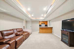 Living room featuring light carpet, recessed lighting, crown molding, a glass covered fireplace, and a tray ceiling