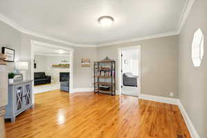 Living room with ornamental molding, light wood-type flooring, and a fireplace