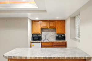 Kitchen with light countertops, brown cabinets, backsplash, dishwasher, and black microwave