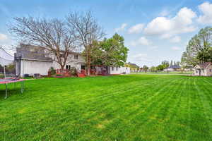 View of green lawn featuring a trampoline and a wooden deck